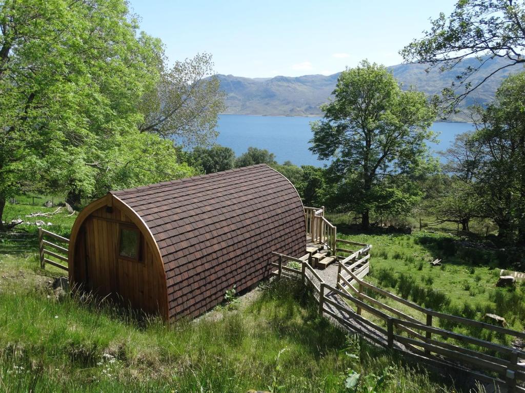 un cobertizo de madera en un campo con una valla y un lago en The Wee Lodge en Mallaig