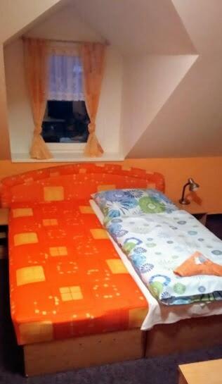 an orange bed in a room with a window at Penzion Zlata studna in Hlinsko