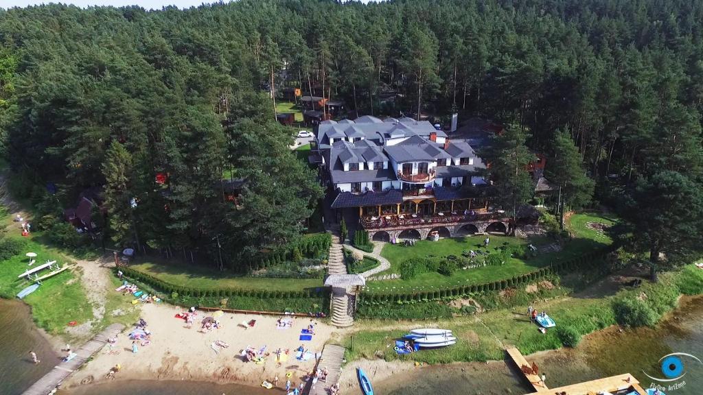 Aerial view of lakeside resort building, sandy beach with sunbathers, and dense surrounding forest.