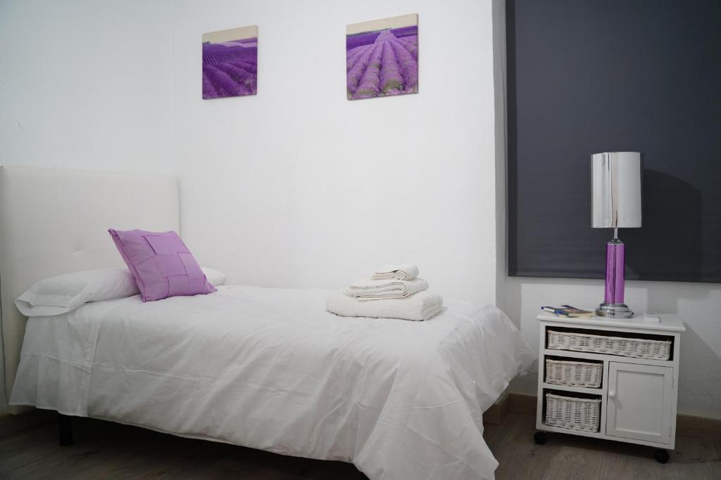 a white bed with purple pillows and a lamp on a table at Apartamento turístico Calle San Basilio 6 patios in Córdoba