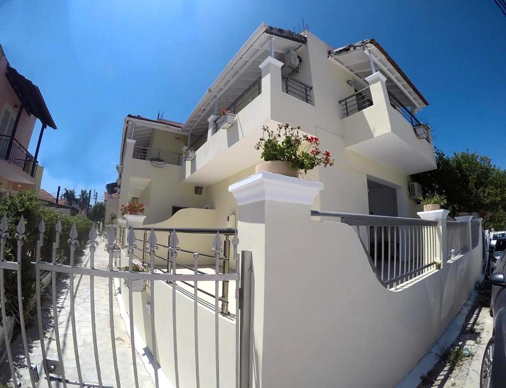 a white building with a fence and flowers on it at Jessica's Studios & Apartments in Kavos