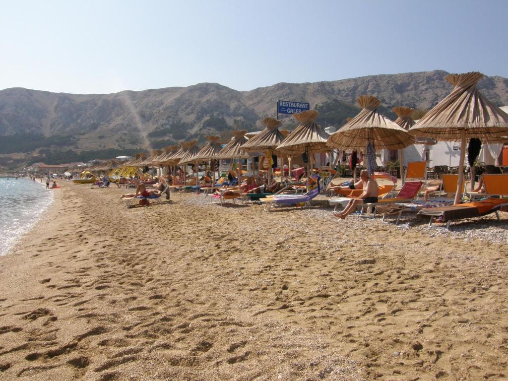 a beach with chairs and umbrellas and people on it at Villas Corinthia in Baška