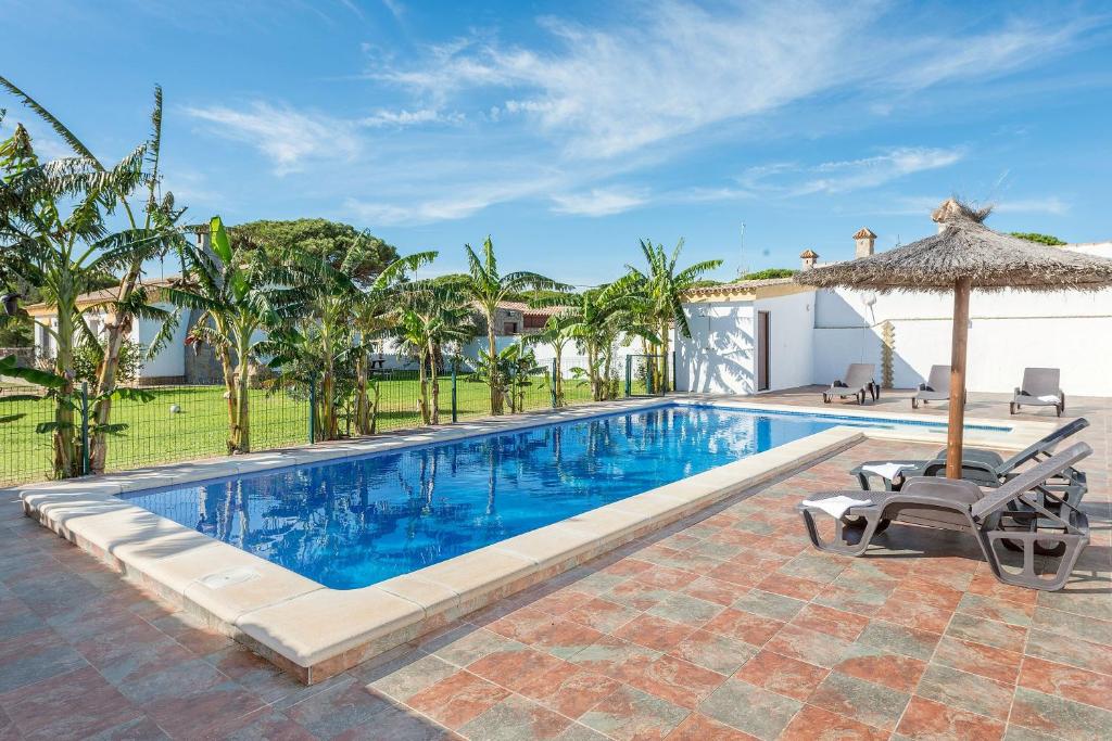 a swimming pool with two chairs and an umbrella at Casa Layda - Sólo Familias in Conil de la Frontera