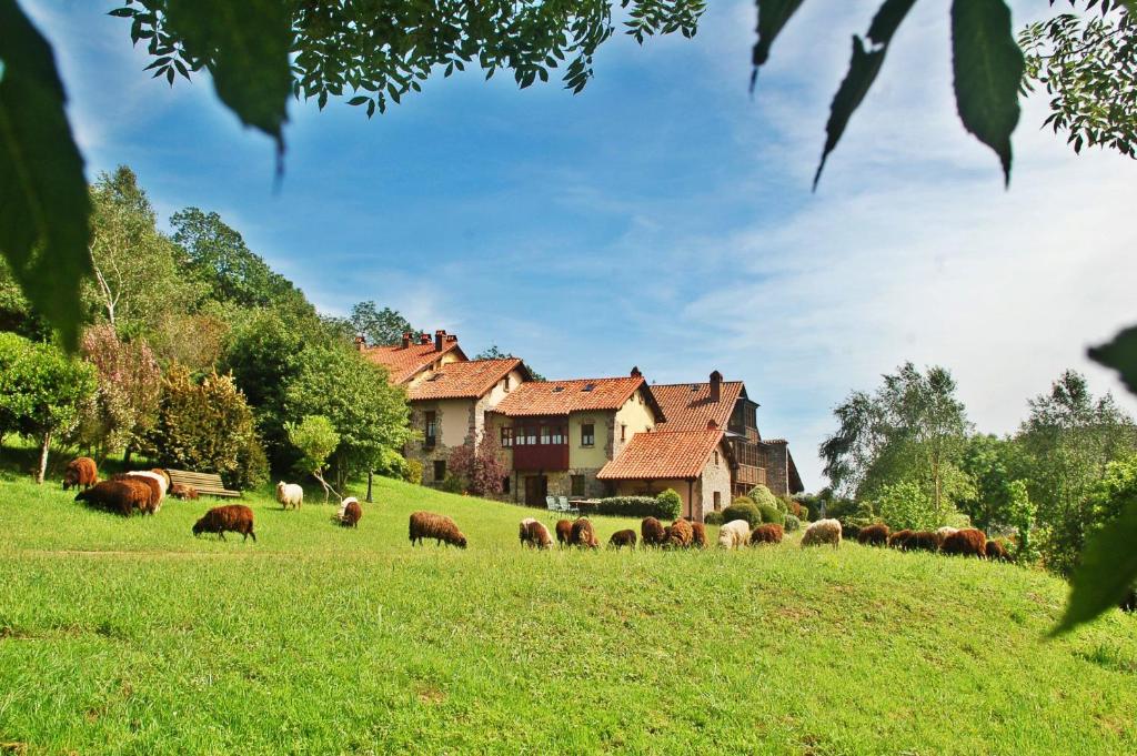 una manada de ganado pastando en un campo frente a una casa en La Montaña Mágica Hotel Rural, en Vibaño