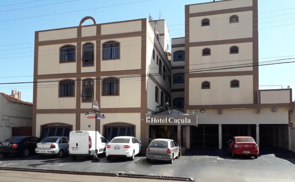 een gebouw met auto's geparkeerd op een parkeerplaats bij Hotel Caçula in Londrina