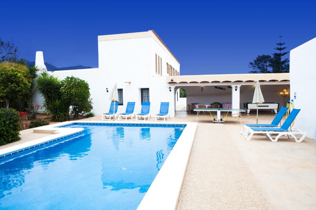 a swimming pool with blue chairs and a house at Can Murenu in Sant Joan de Labritja