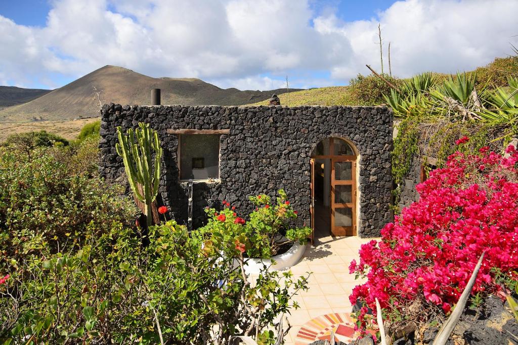 un pequeño edificio de piedra con flores delante en La Bodega - House on volcano with a piano, en Haría
