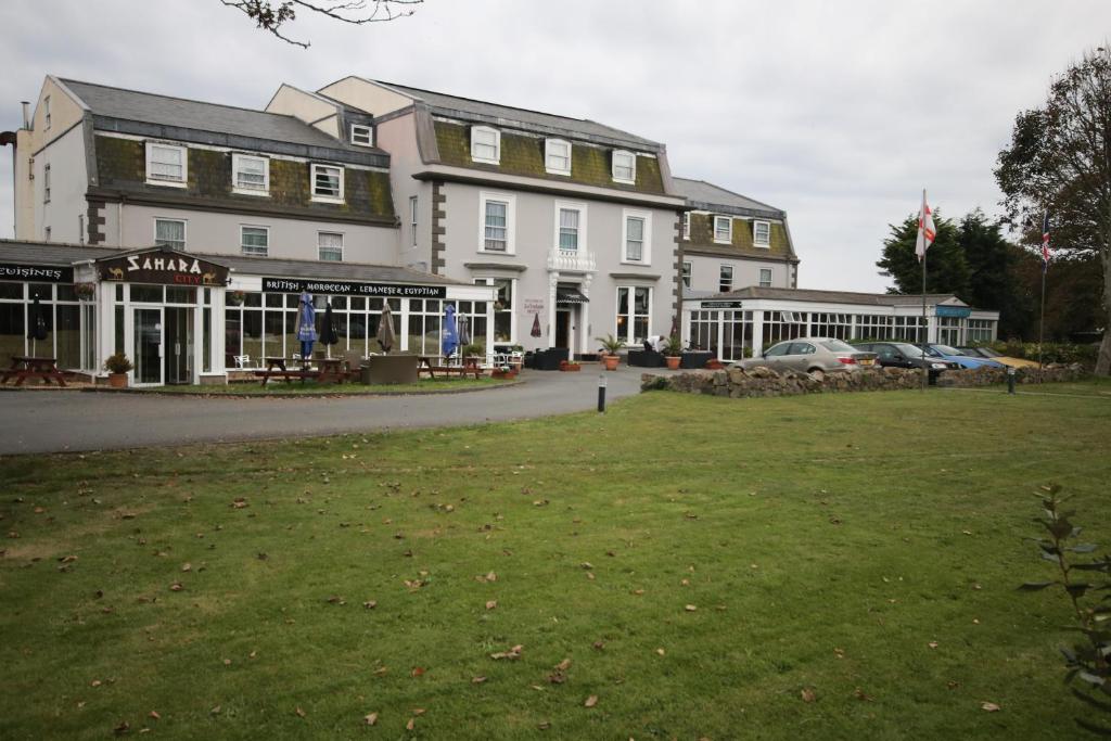 un gran edificio con un césped verde delante de él en La Trelade Hotel en St Martin Guernsey