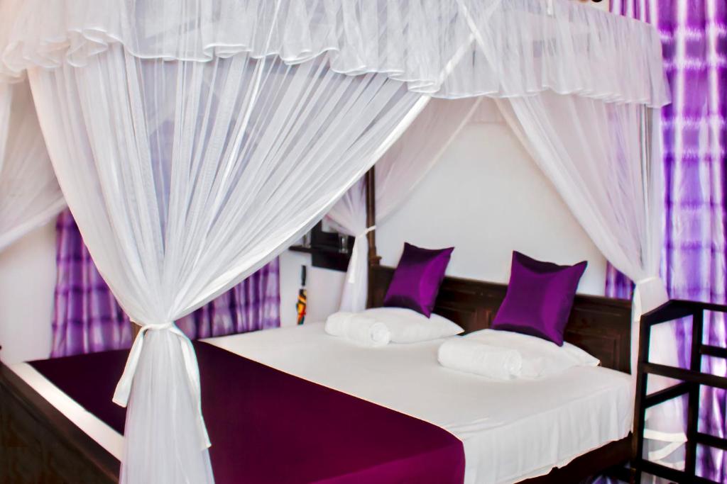 a bedroom with a canopy bed with purple curtains at Star Light Cabanas & Restaurant in Tangalle