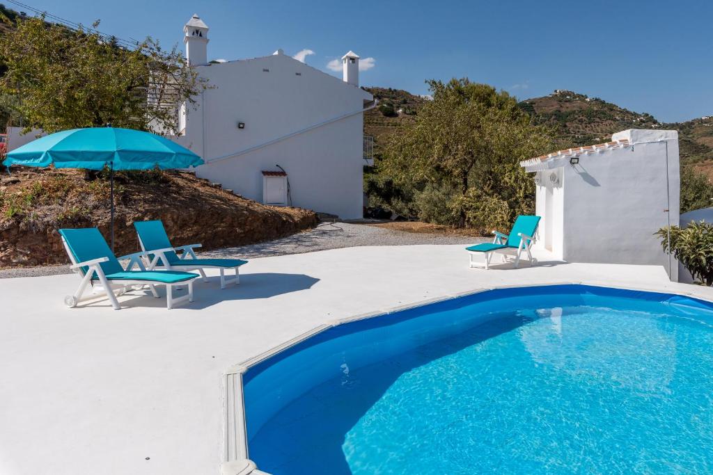 einem Pool mit Stühlen und einem Sonnenschirm neben einem Haus in der Unterkunft Villa Felicidad destino romántico in Sayalonga