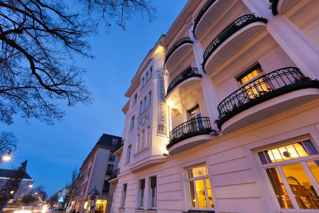 ein großes weißes Gebäude mit Balkon in einer Stadtstraße in der Unterkunft Hotel Herzoghof in Baden