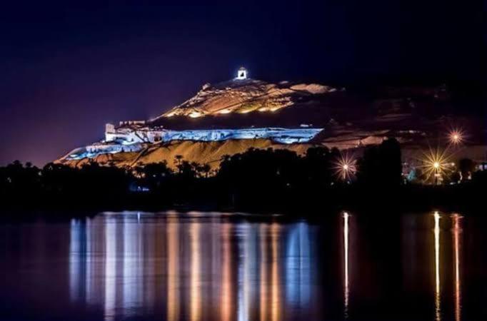 an island in the water at night with lights at Kosh royal house in Aswan