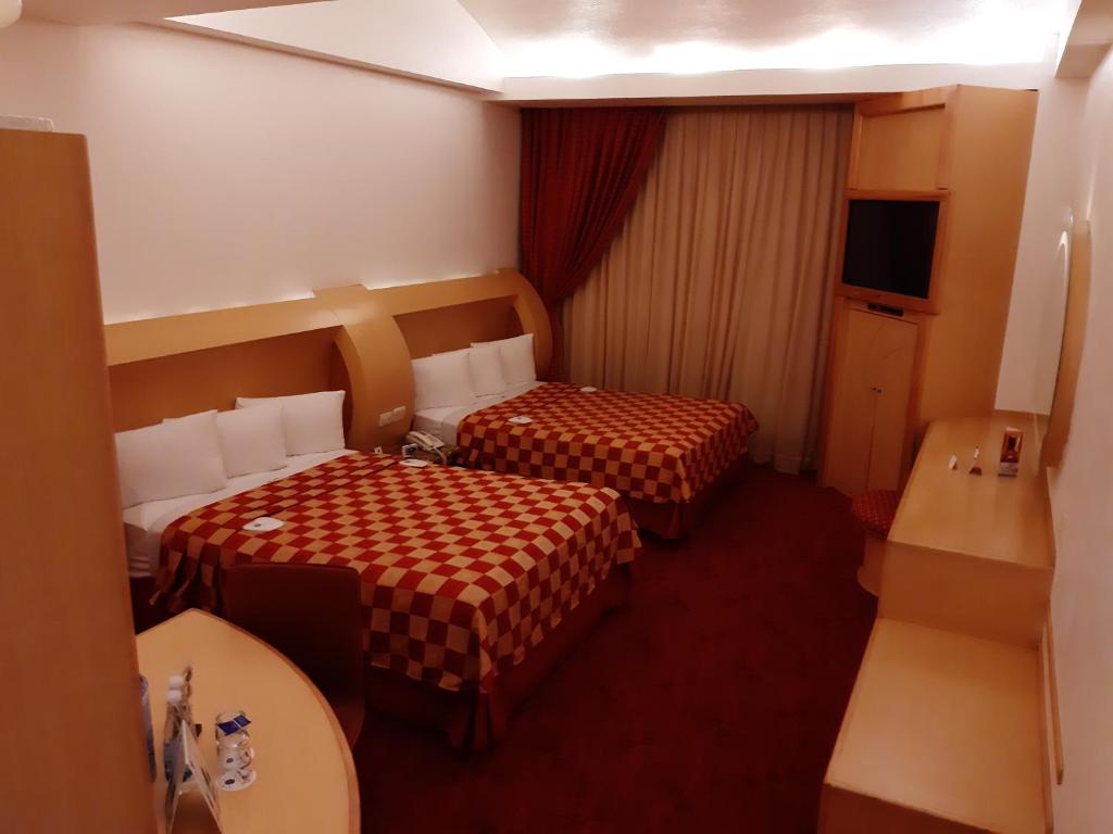 A two-bed room with a curtained window, built-in television and long wood work surface.