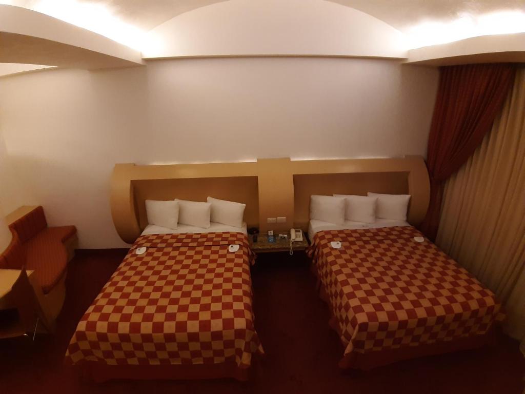A two-bed room with a central bedside table, red carpet and upholstered corner seating.