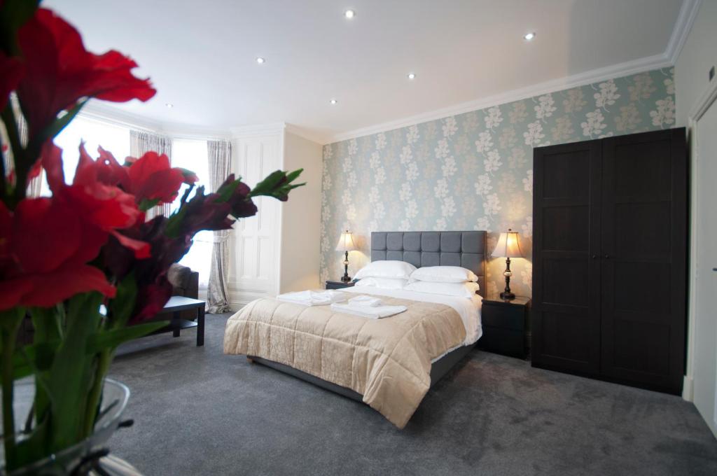 a bedroom with a bed and a vase of red flowers at Palmerston Suites in Edinburgh