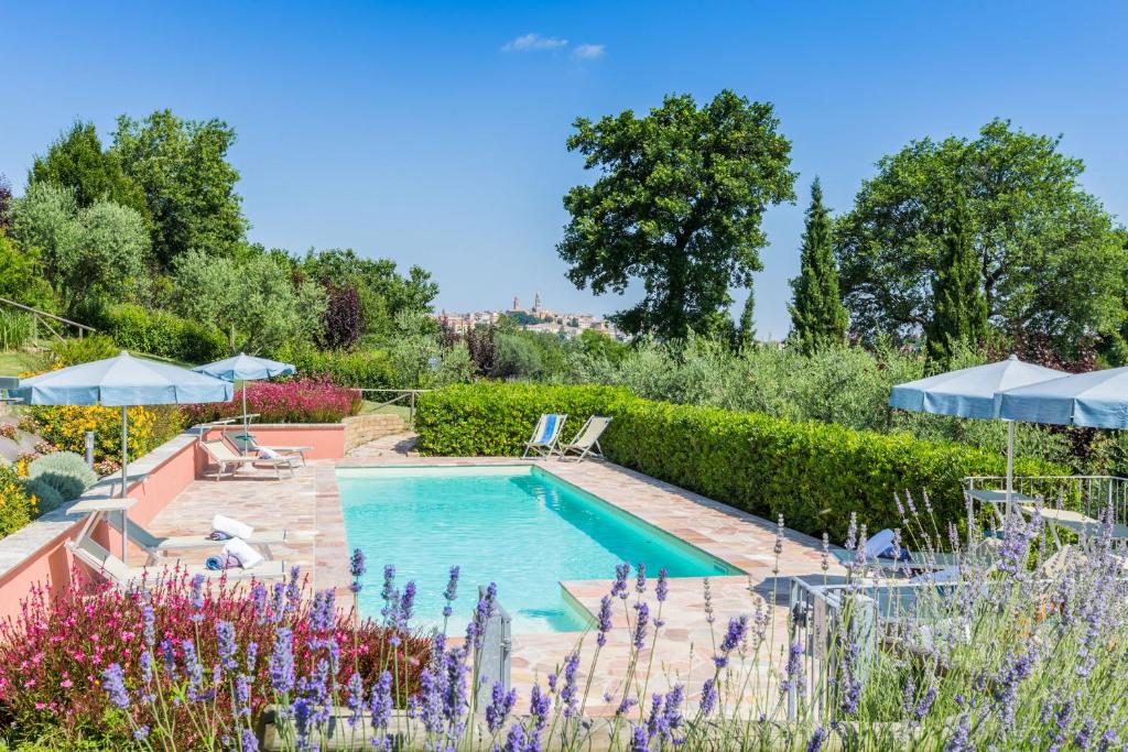 una piscina en un jardín con flores y sombrillas en Villa Azzurra en Mondavio