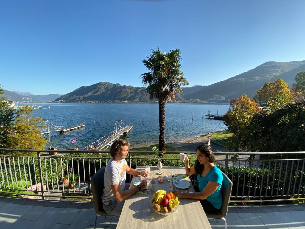 two people sitting at a table with a view of the water at apartment Lac Brusimpiano in Brusimpiano