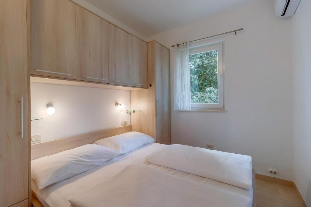 a bedroom with a white bed and a window at Apartments Pineta in Cunski