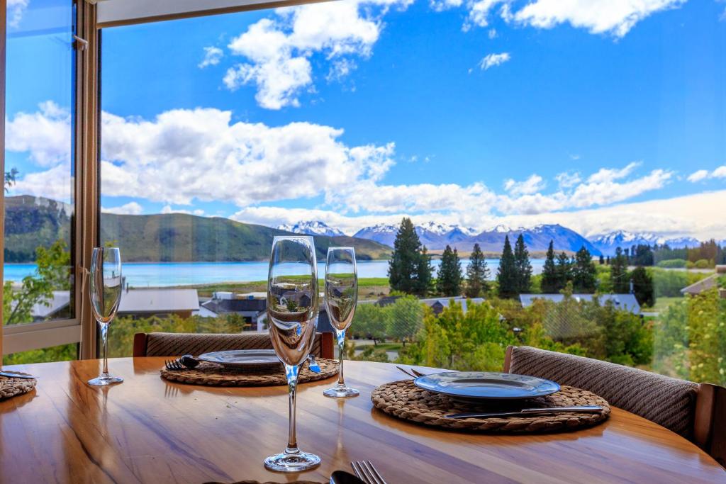 a table with wine glasses and a view of the mountains at Glacier Rock Lakeview House in Lake Tekapo