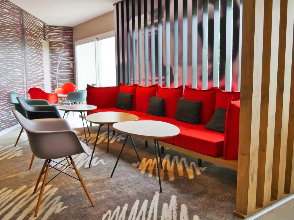 a red couch in a room with tables and chairs at ibis Laval Le Relais D'Armor in Laval