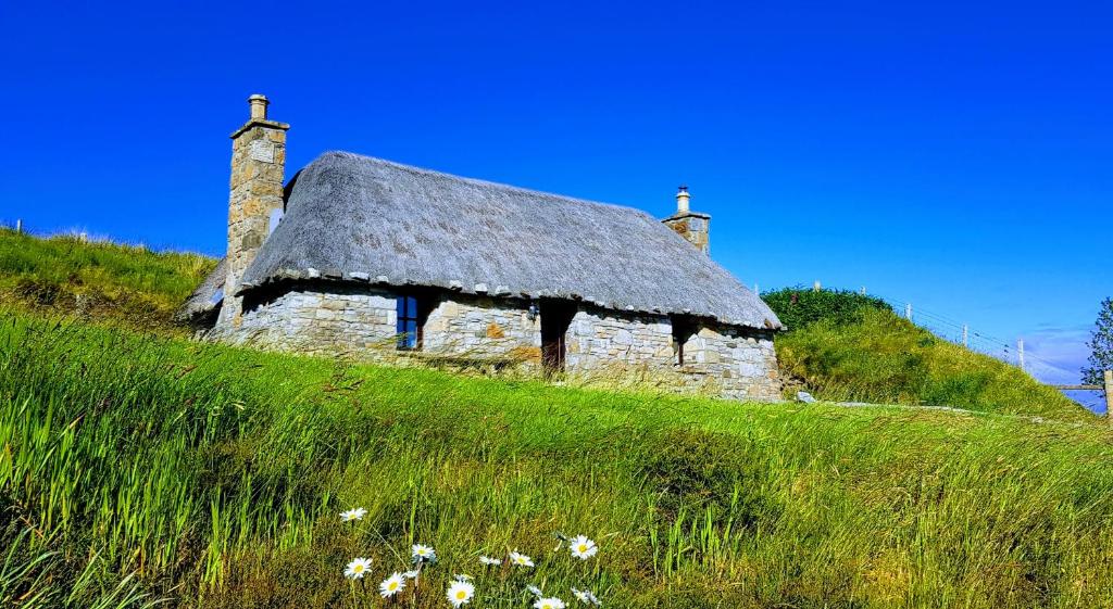 an old stone house with a thatched roof on a hill at Tigh Lachie at Mary's Thatched Cottages, Elgol, Isle of Skye in Elgol