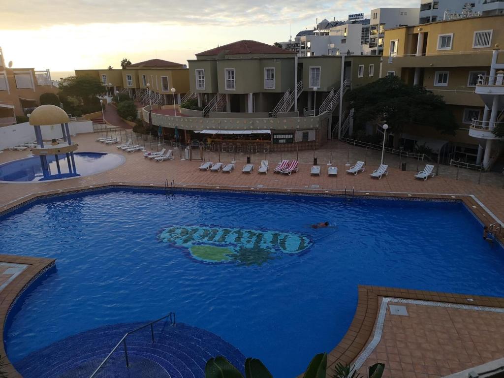 a large blue swimming pool with chairs and buildings at ORLANDO RESORT Playa Las Américas in Adeje