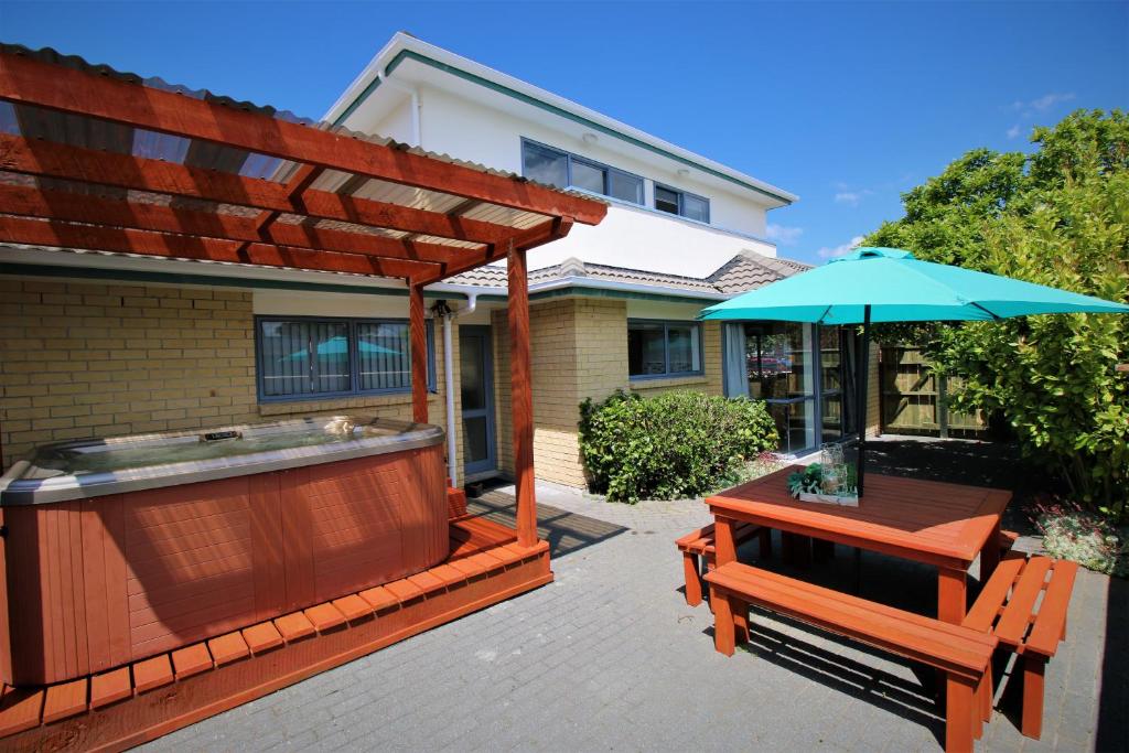 un patio con bañera de hidromasaje, mesa y sombrilla en AristaAir- Central City Townhouse en Rotorua