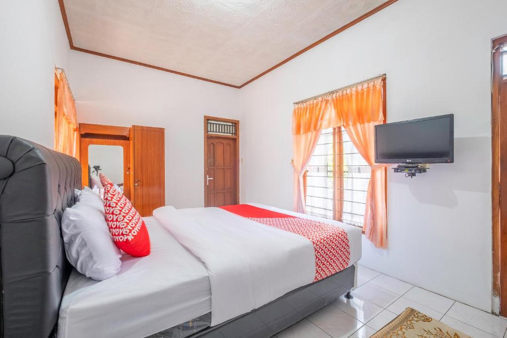 1 dormitorio con 1 cama con almohadas rojas y TV en Capital O 1541 Puri Cikole Asri, en Lembang