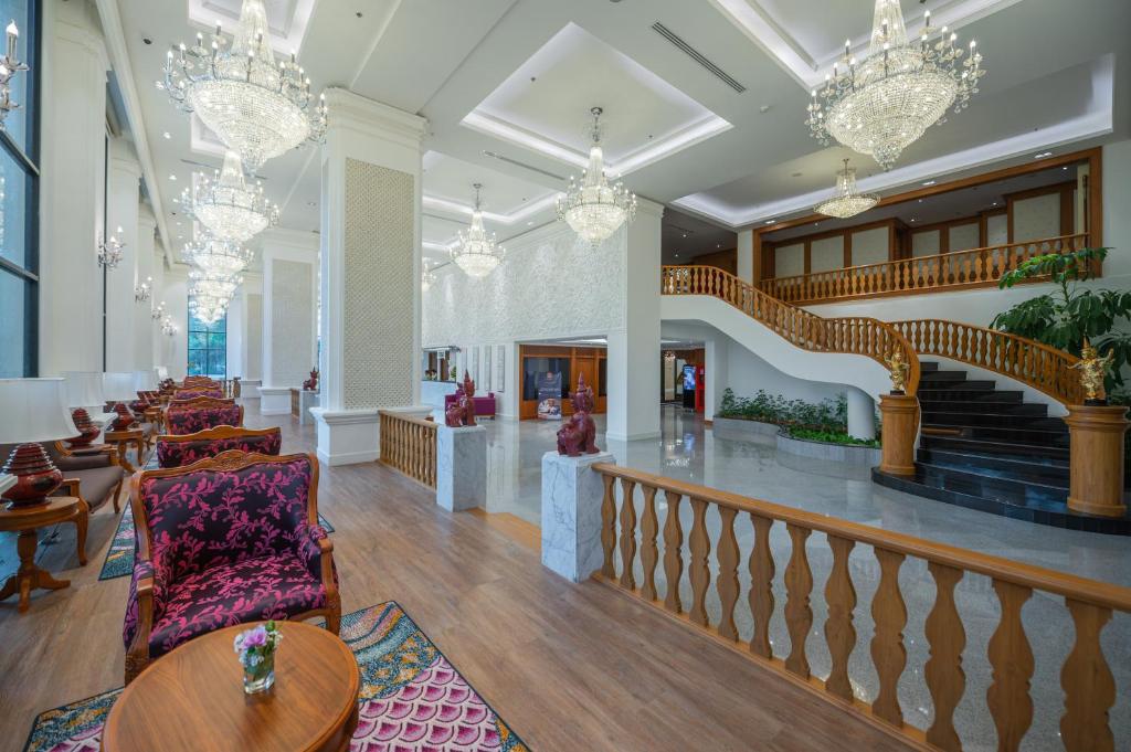 A grand lobby opens around a curved staircase, chandeliers, and patterned lounge seating.