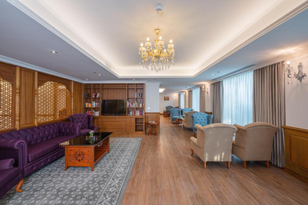A formal lounge features purple sofas, upholstered chairs, bookshelves, and chandeliers.