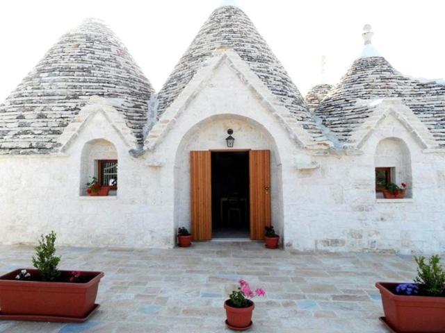 a white building with a door and some potted plants at Il trullo del Mirto in Selva di Fasano