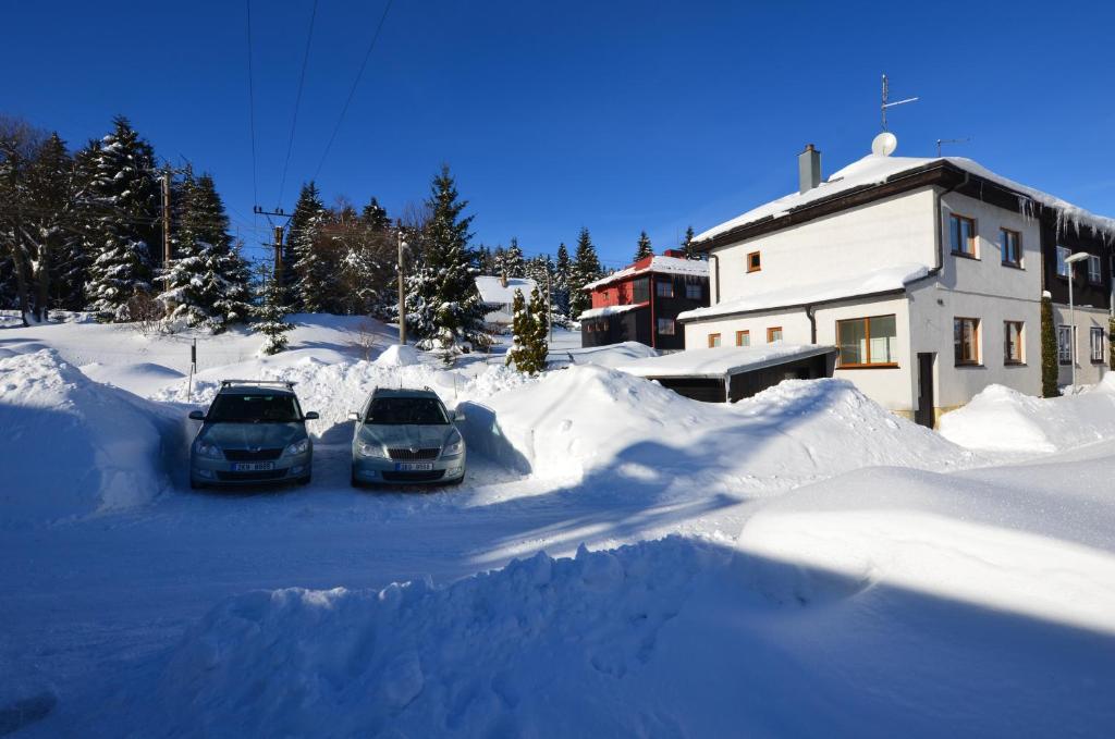 zwei Autos auf einem schneebedeckten Parkplatz in der Unterkunft Naproti Klínovci in Jáchymov