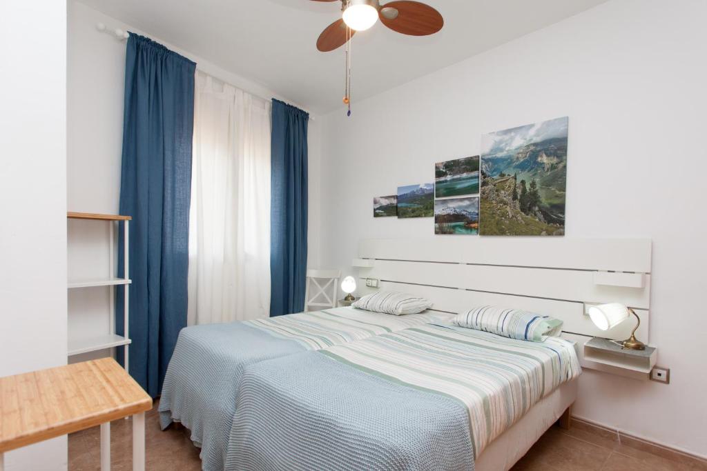 a white bedroom with a bed with blue curtains at Casa Bubal by Best Holidays Fuerteventura in Corralejo