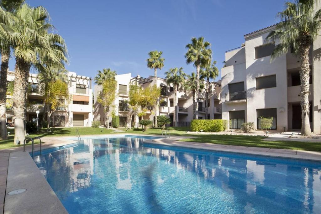 una piscina con palmeras frente a un edificio en La Roza de Roda Golf en San Javier
