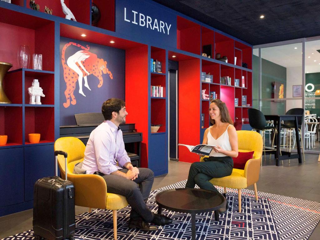 a man and woman sitting in chairs in a library at Aparthotel Adagio Basel City in Basel