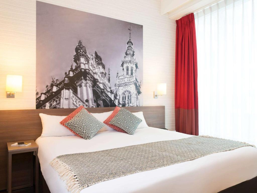 Schlafzimmer mit einem großen weißen Bett und roten Vorhängen in der Unterkunft Aparthotel Adagio Brussels Grand Place in Brüssel