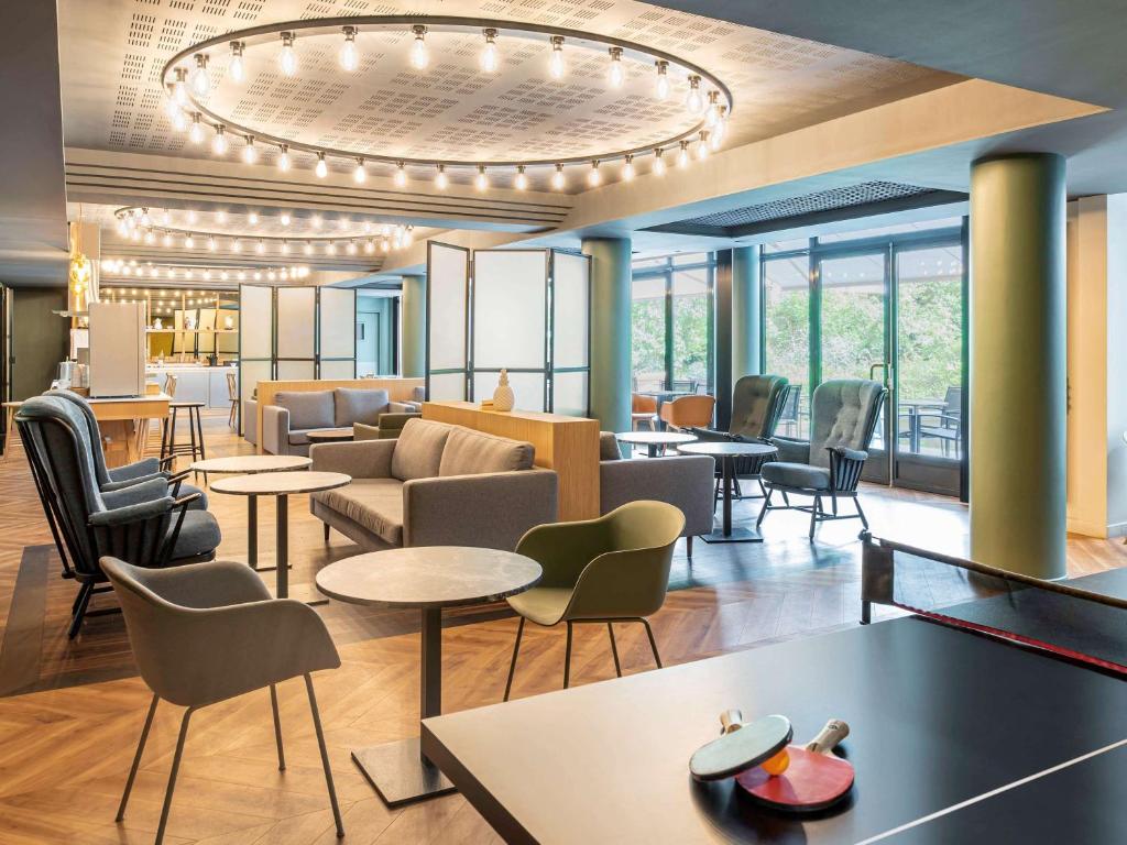 Le hall de l'hôtel est doté de tables, de chaises et d'un lustre. dans l'établissement Aparthotel Adagio Porte de Versailles, à Paris