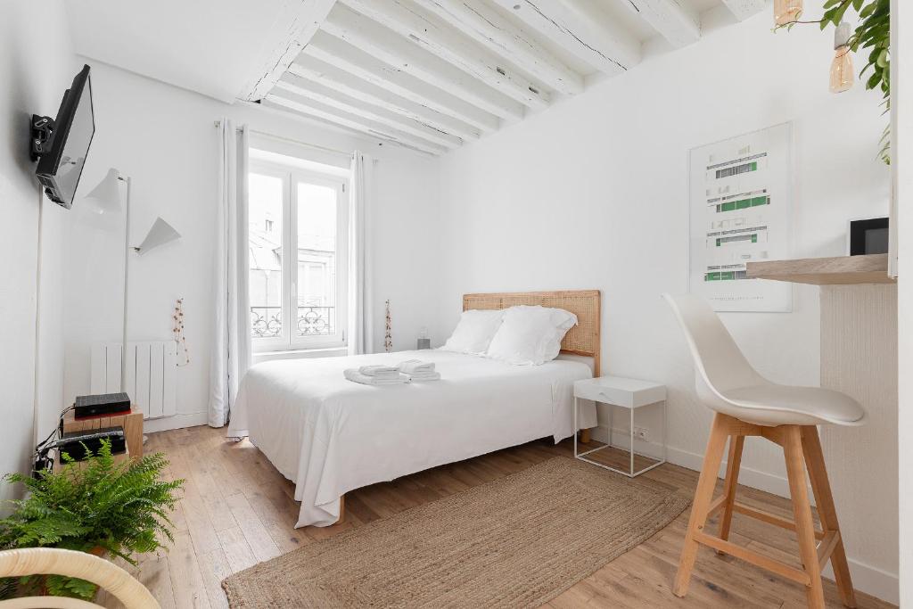 a white bedroom with a white bed and a chair at Appartement Vertus in Paris