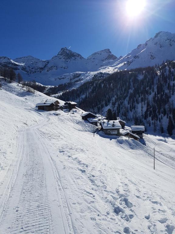 une montagne enneigée avec une piste de ski avec des bâtiments dans l'établissement L' Aroula Rooms & Restaurant, à Champoluc