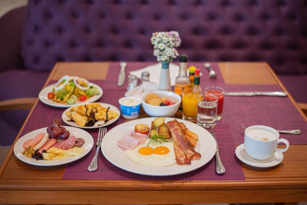 A fully set breakfast table with eggs, bacon, fruit, pastries, drinks, and coffee.