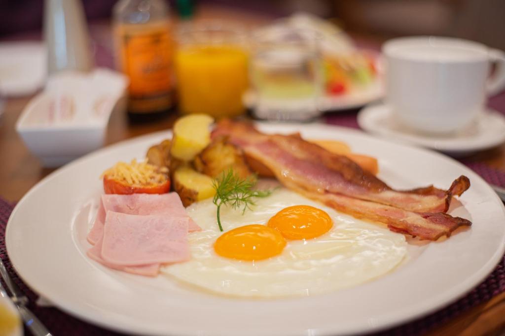 A close-up cooked breakfast plate with eggs, bacon, ham, potatoes, and vegetables.