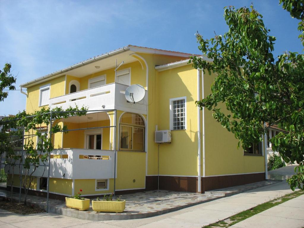una casa gialla e bianca con un albero di Apartments Polonijo a Baška