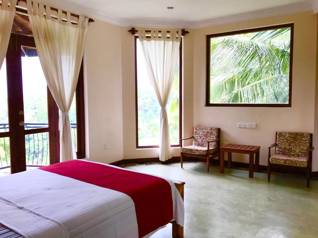 a bedroom with a bed and two chairs and windows at Mount Haven in Kandy