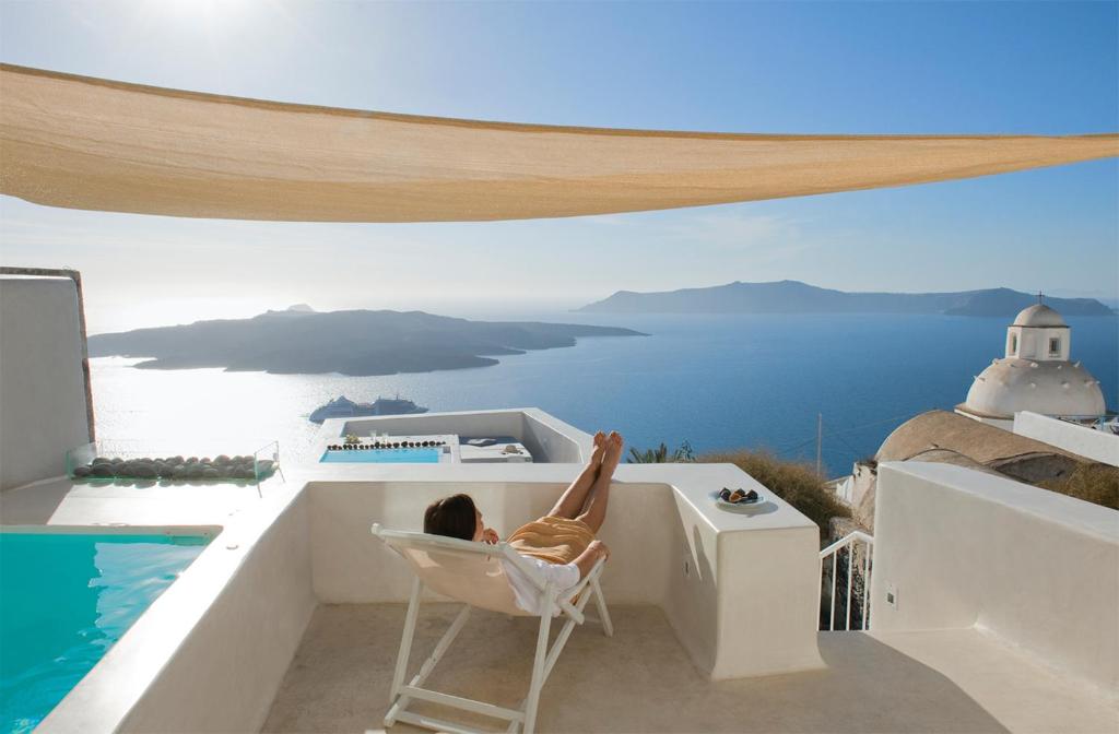 a woman sitting in a chair on a balcony overlooking the ocean at Aesthesis Boutique Villas Fira in Fira