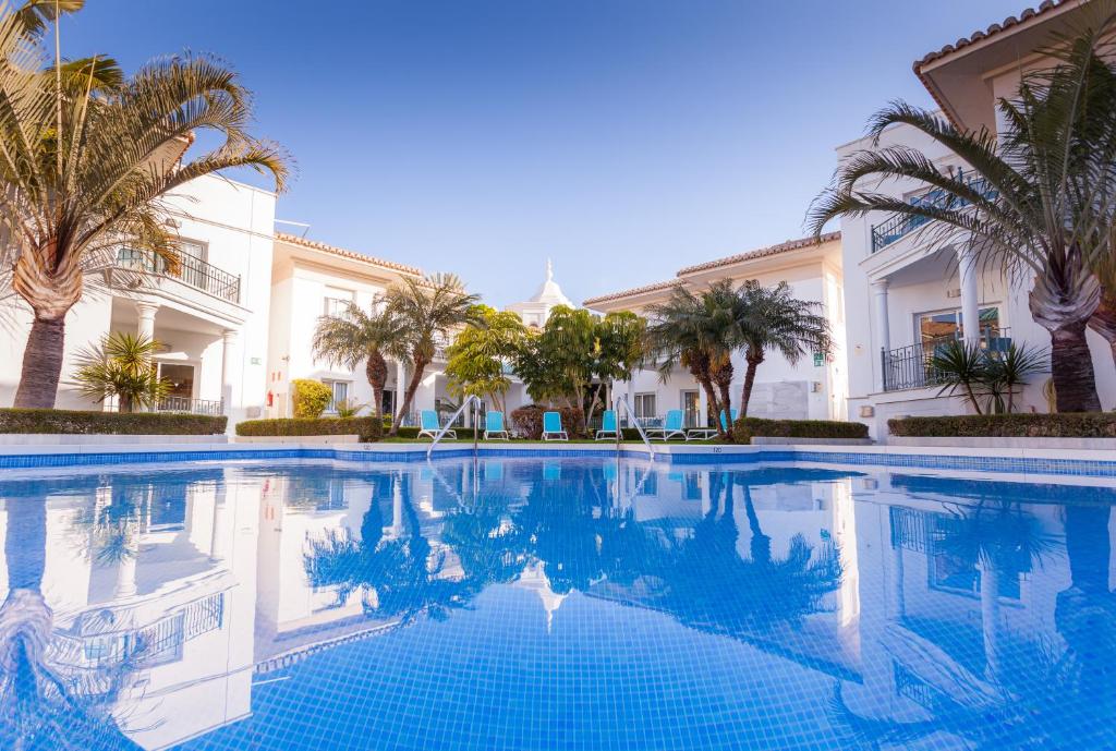 a swimming pool with palm trees in front of a building at Apartamentos Marina Turquesa in Nerja