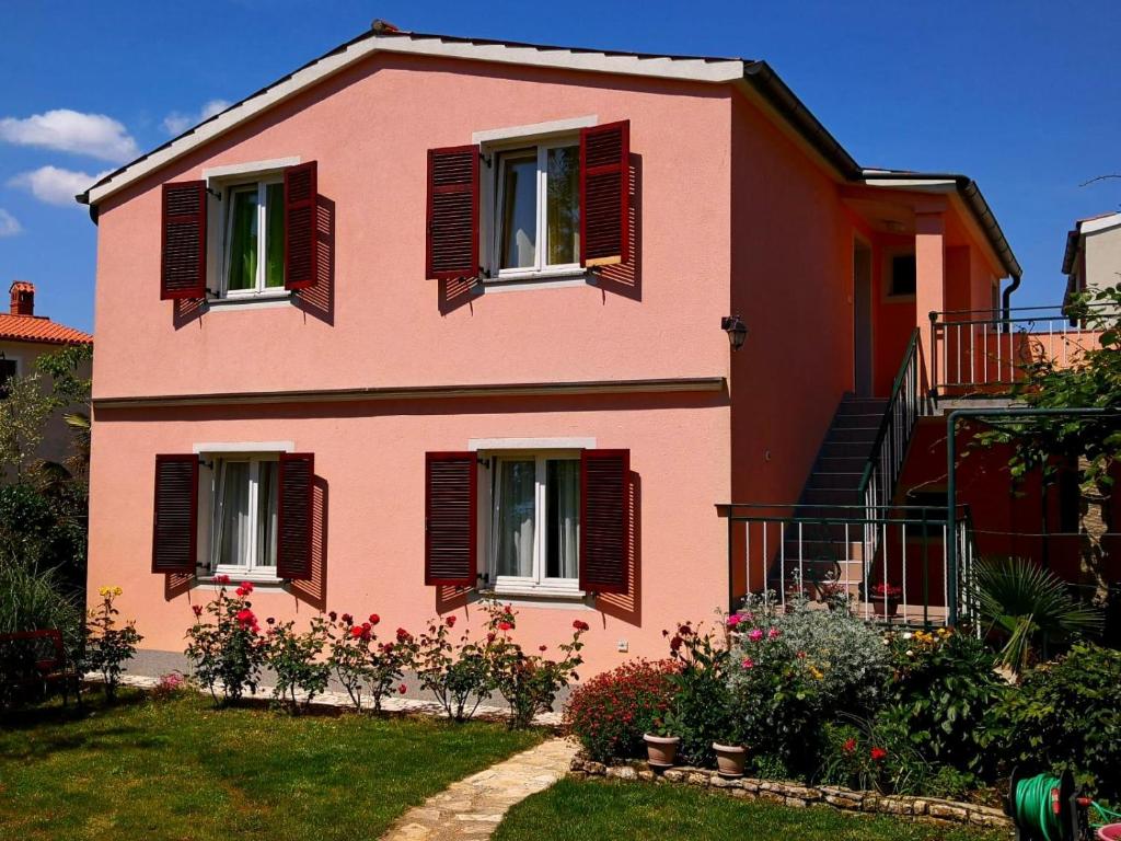 a pink house with red shuttered windows and a yard at Apartments Ines in Medulin