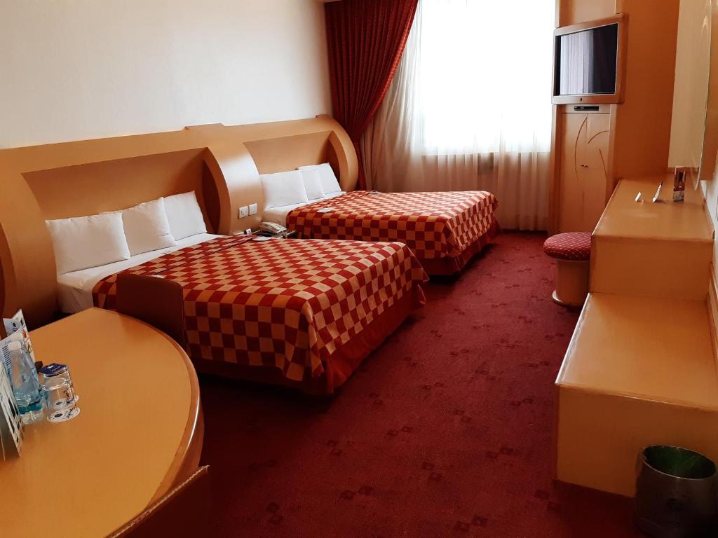 A two-bed room with a built-in desk, vanity, television cabinet and curtained window.