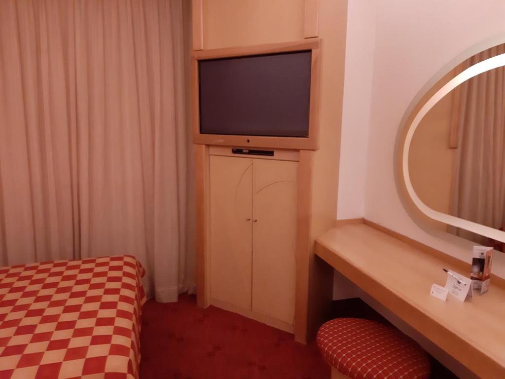A compact vanity desk with a cushioned stool sits beside the television and curtains in the guest room.