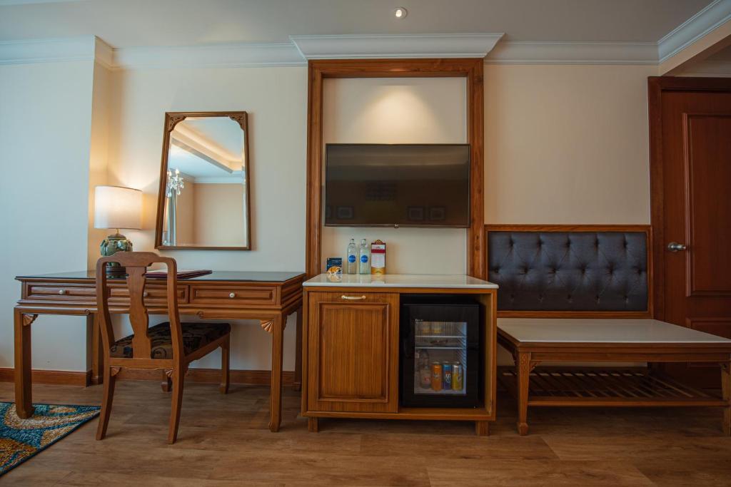 A compact wooden writing desk beside a minibar, television, and upholstered bench.