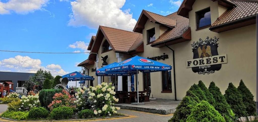 ein Restaurant mit blauen Sonnenschirmen vor einem Gebäude in der Unterkunft Zajazd Forest in Węgrów